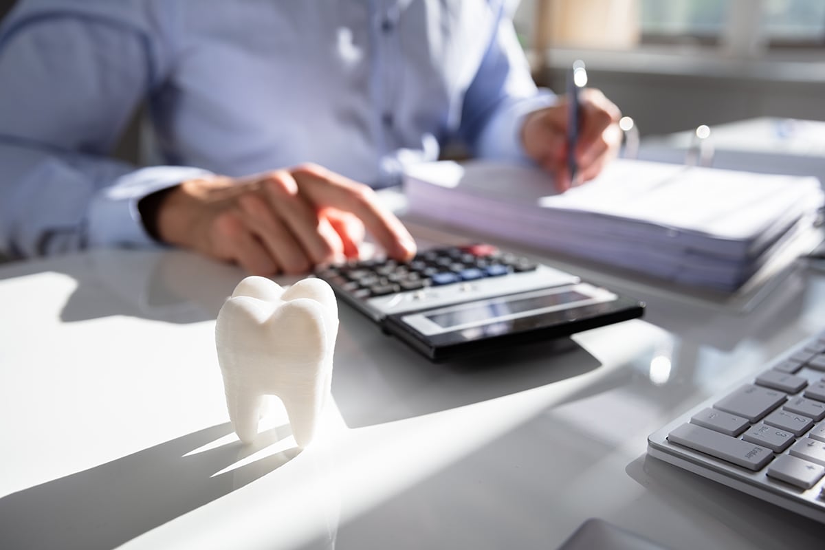 Close-up Of Tooth In Front Of Businessperson Calculating Bill